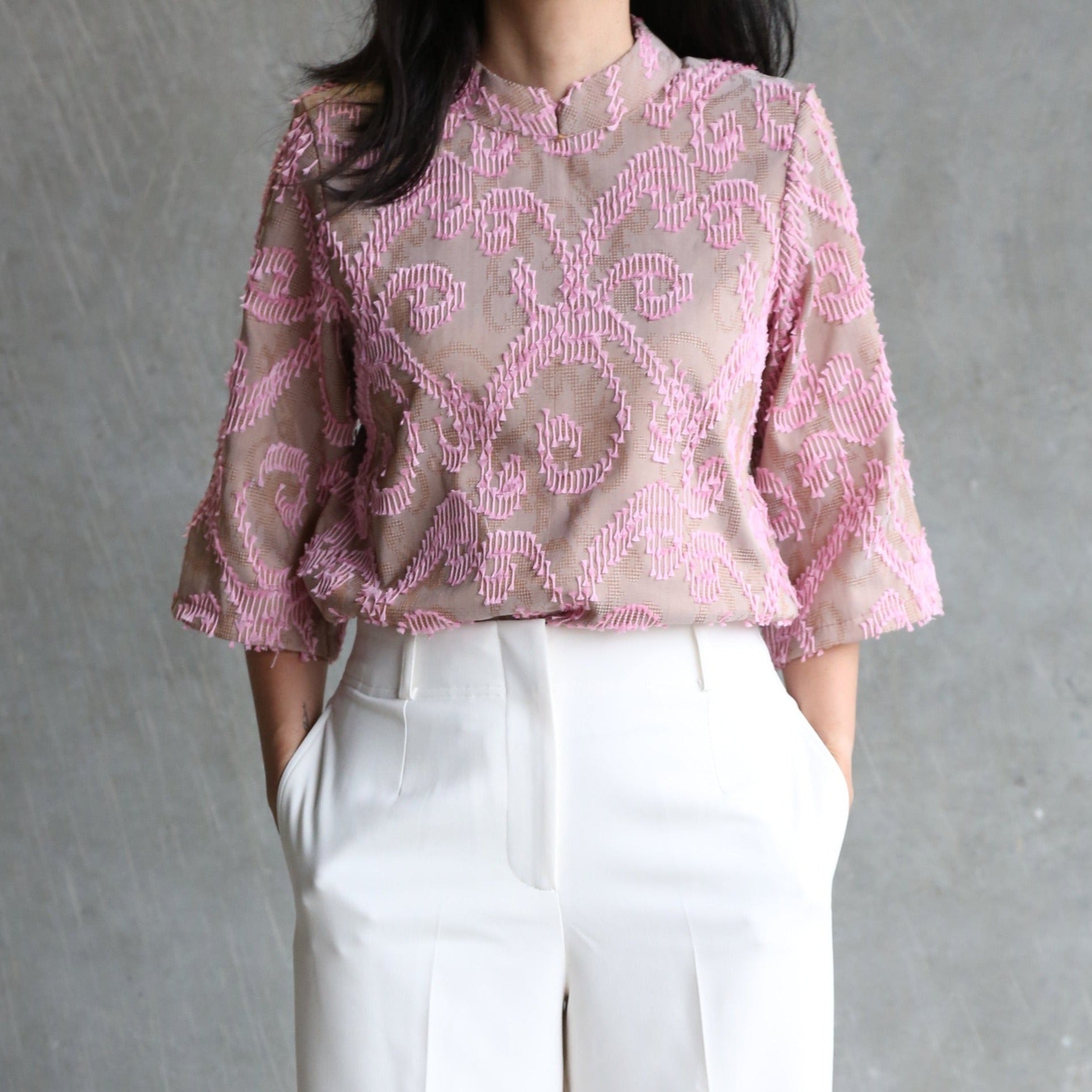 A person wearing a high-neck pink and green Ling shanghai top with handwoven heritage fabric and white trousers.