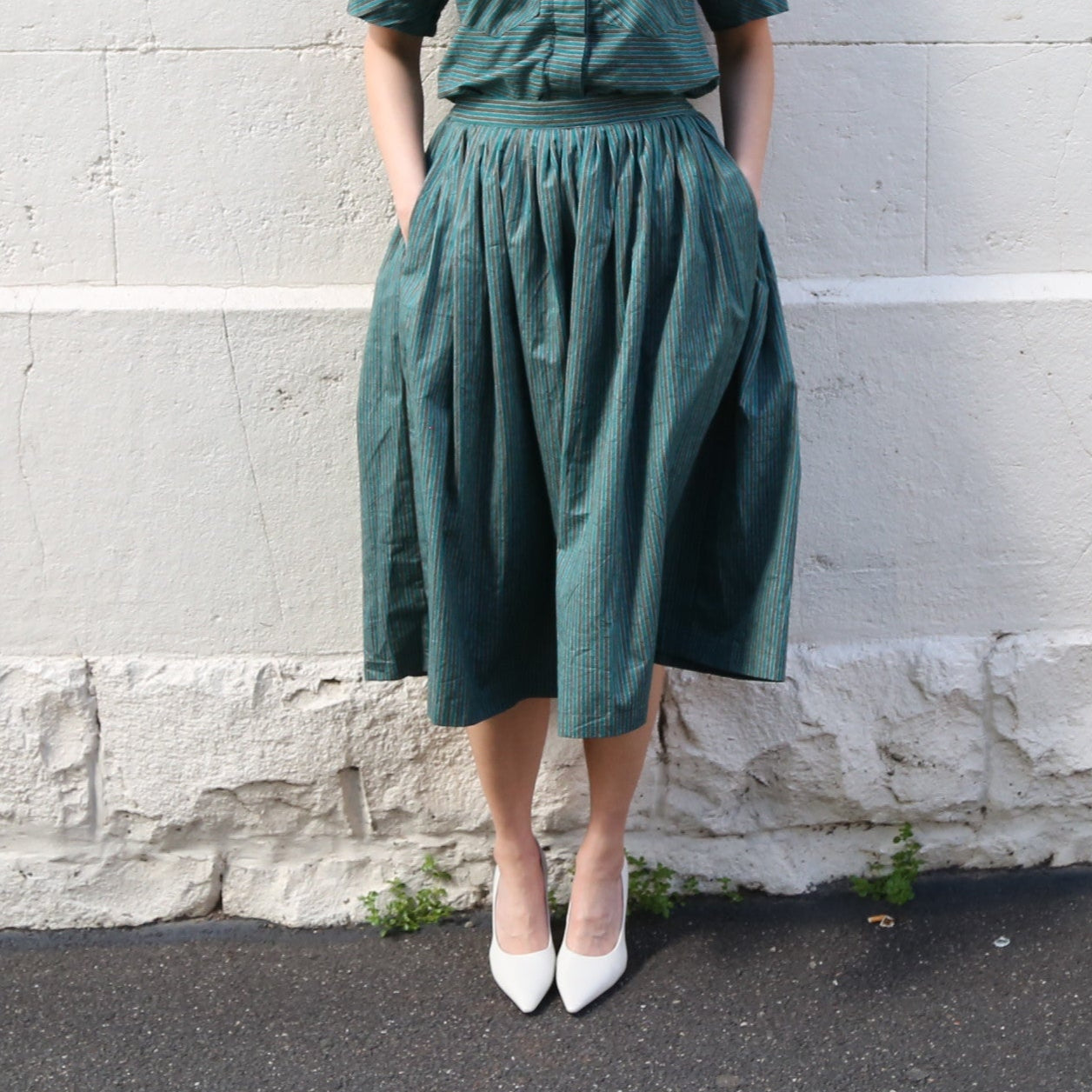 Person wearing a green skirt and white shoes against a gray wall.