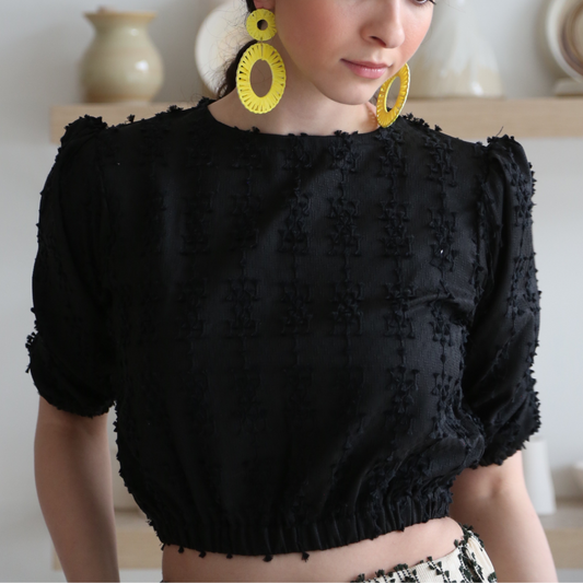 A woman wearing a black olive top with cropped puffed sleeves and a stretchy hem, paired with yellow earrings.
