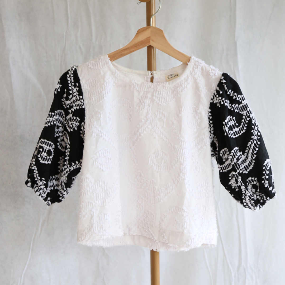 White blouse with black patterned sleeves on a wooden hanger against a white background