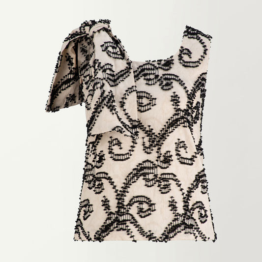 Sleeveless top with a dramatic bow at the one shoulder and a round neckline, featuring a pattern of black feathers on a beige base.