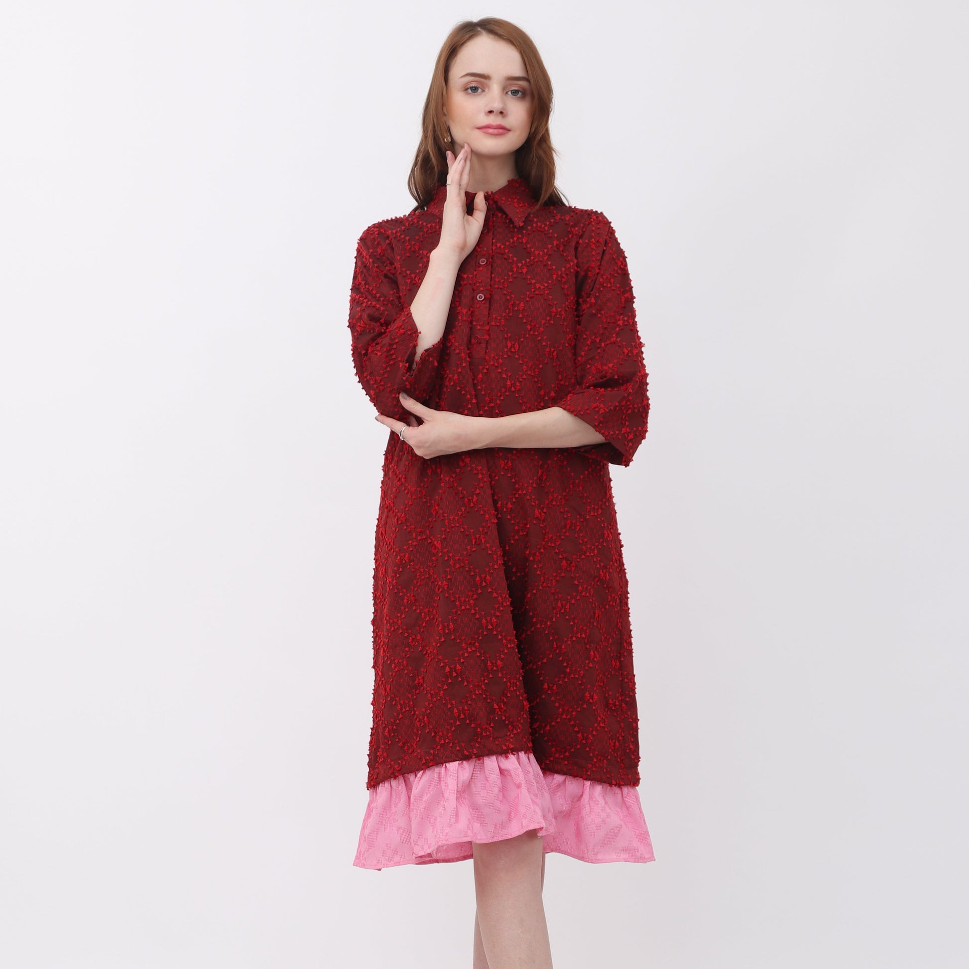 A woman standing against a white background wearing a red Luna shirt dress with a ruffled hem and side pockets.