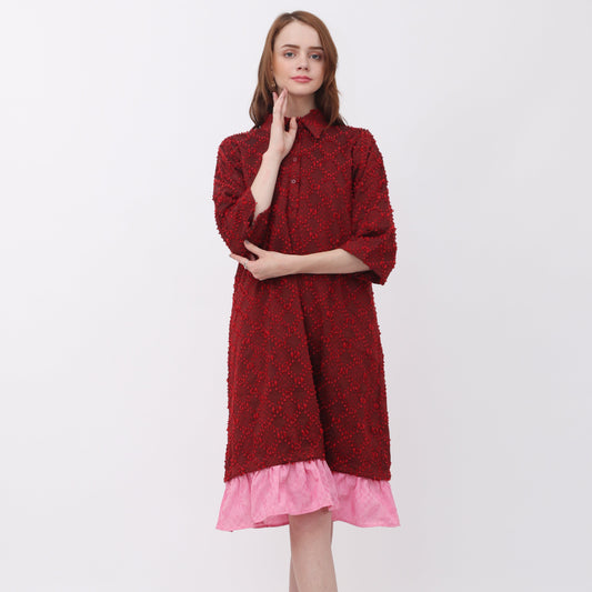 A woman standing against a white background wearing a red Luna shirt dress with a ruffled hem and side pockets.