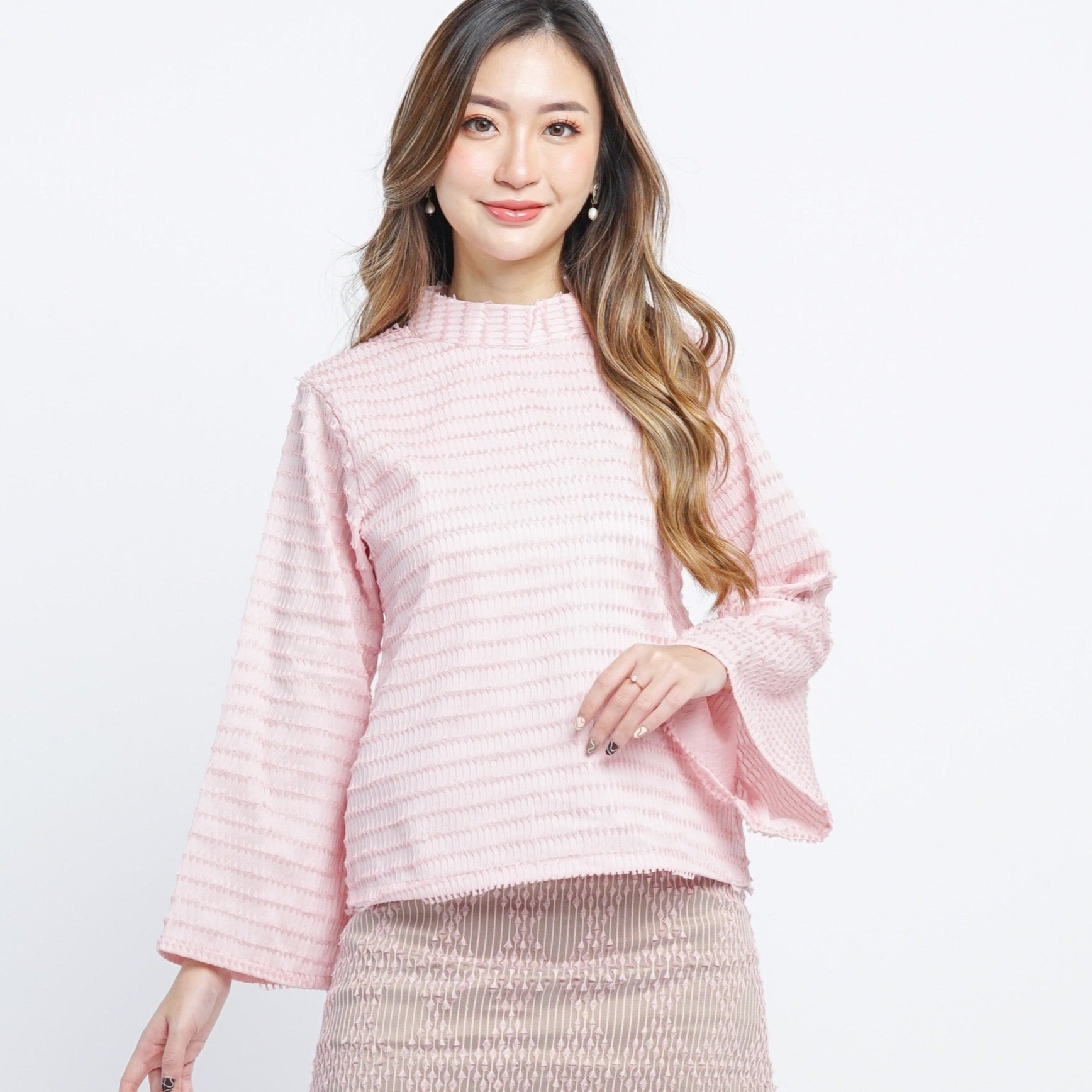 A woman wearing a traditional beige blush long sleeves top with a high neck, made with handwoven tenun fabric.