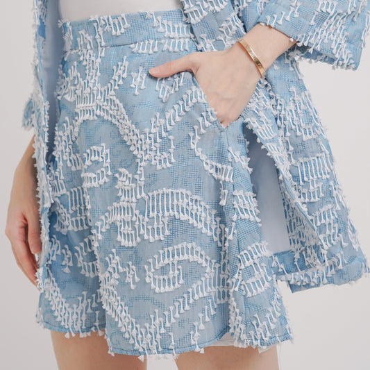 High-waisted blue and white tenun shorts with a feathery accent, displayed on a person from the back, showcasing the fit and design of the garment.