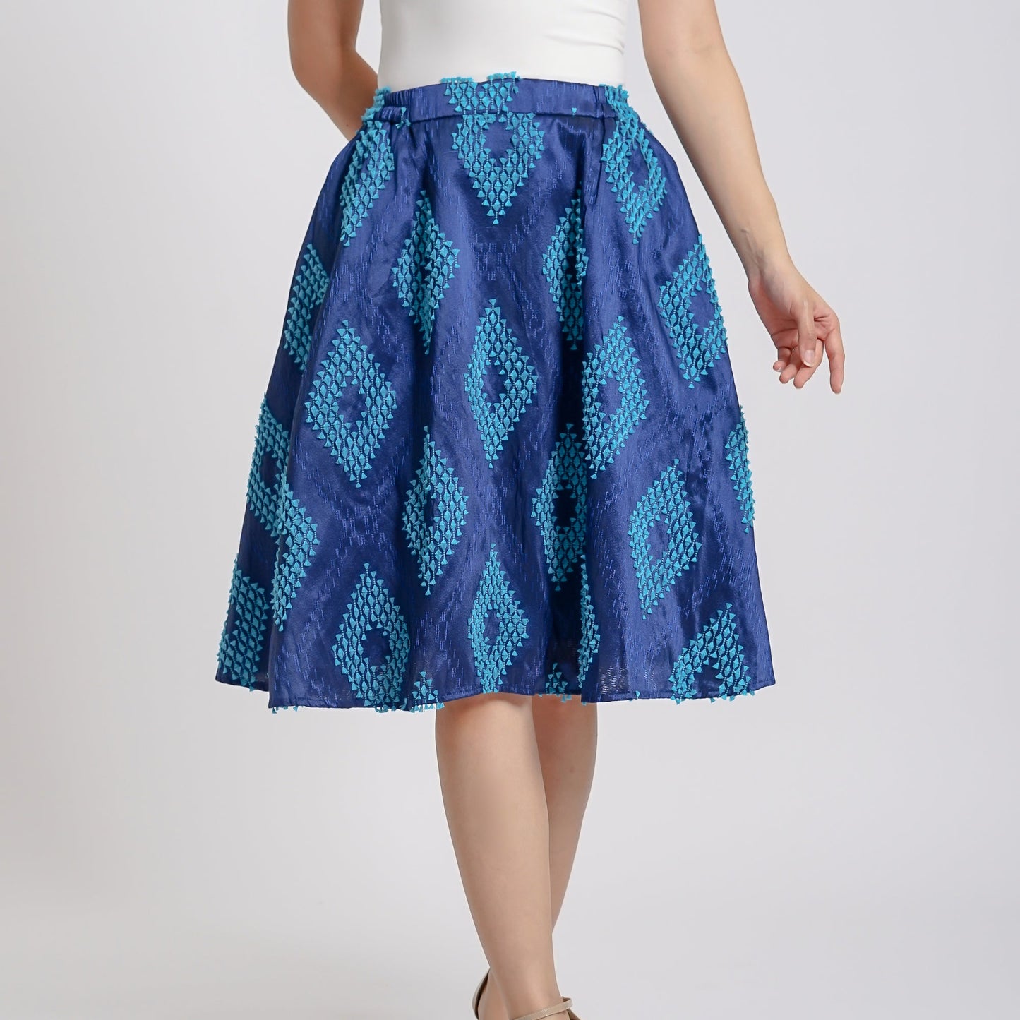 A woman wearing a blue and white geometric patterned skirt with a stretchy waistband, paired with a white top and beige sandals.
